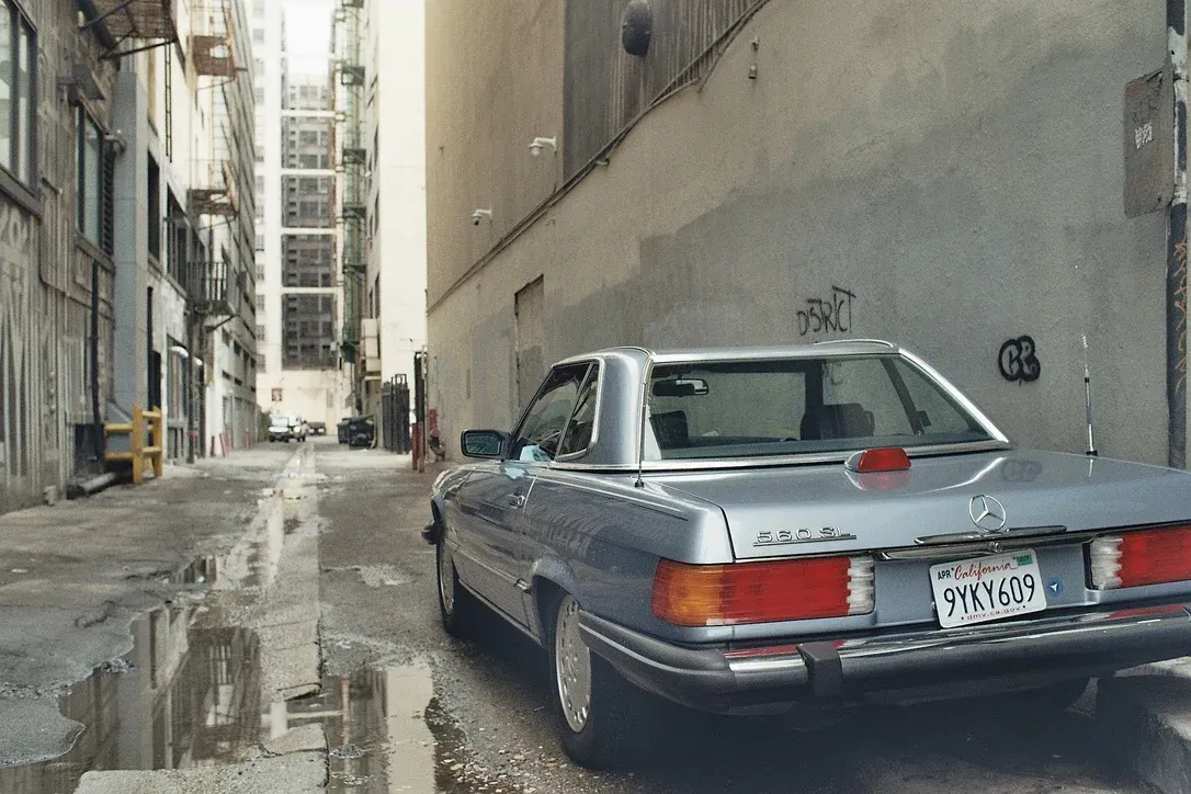 Vintage silver Mercedes parked in an alleyway with puddles and graffiti in Los Angeles